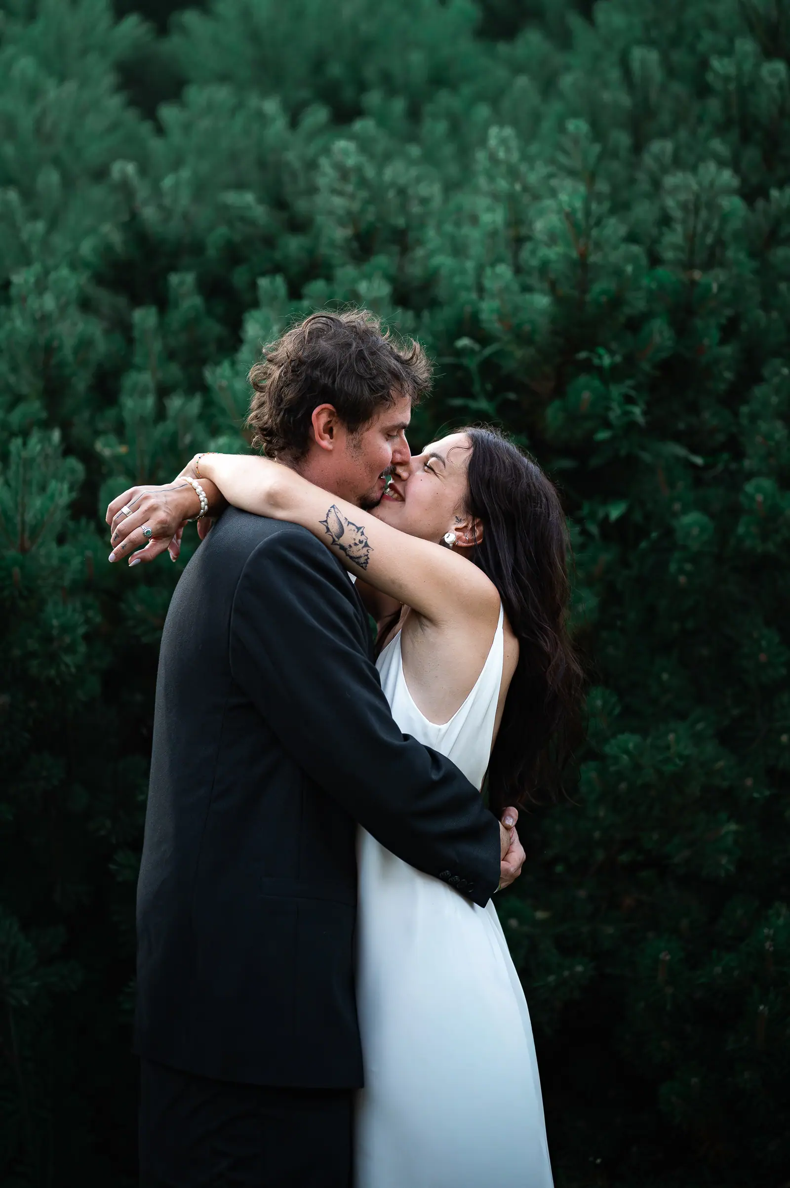 Couple kissing in front of dark green hedges
