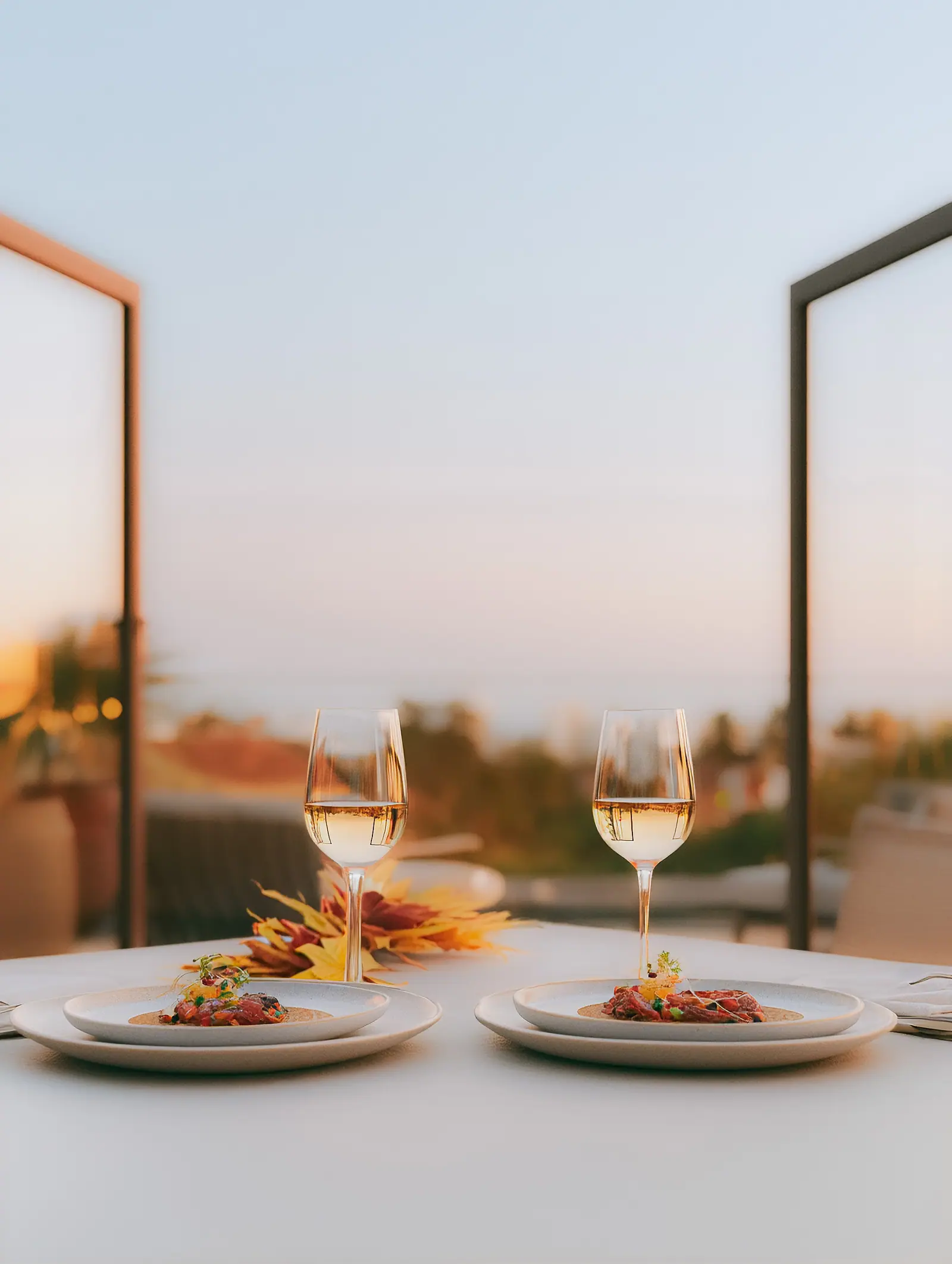 Two plates and glasses of white wine on a terrace at sunset