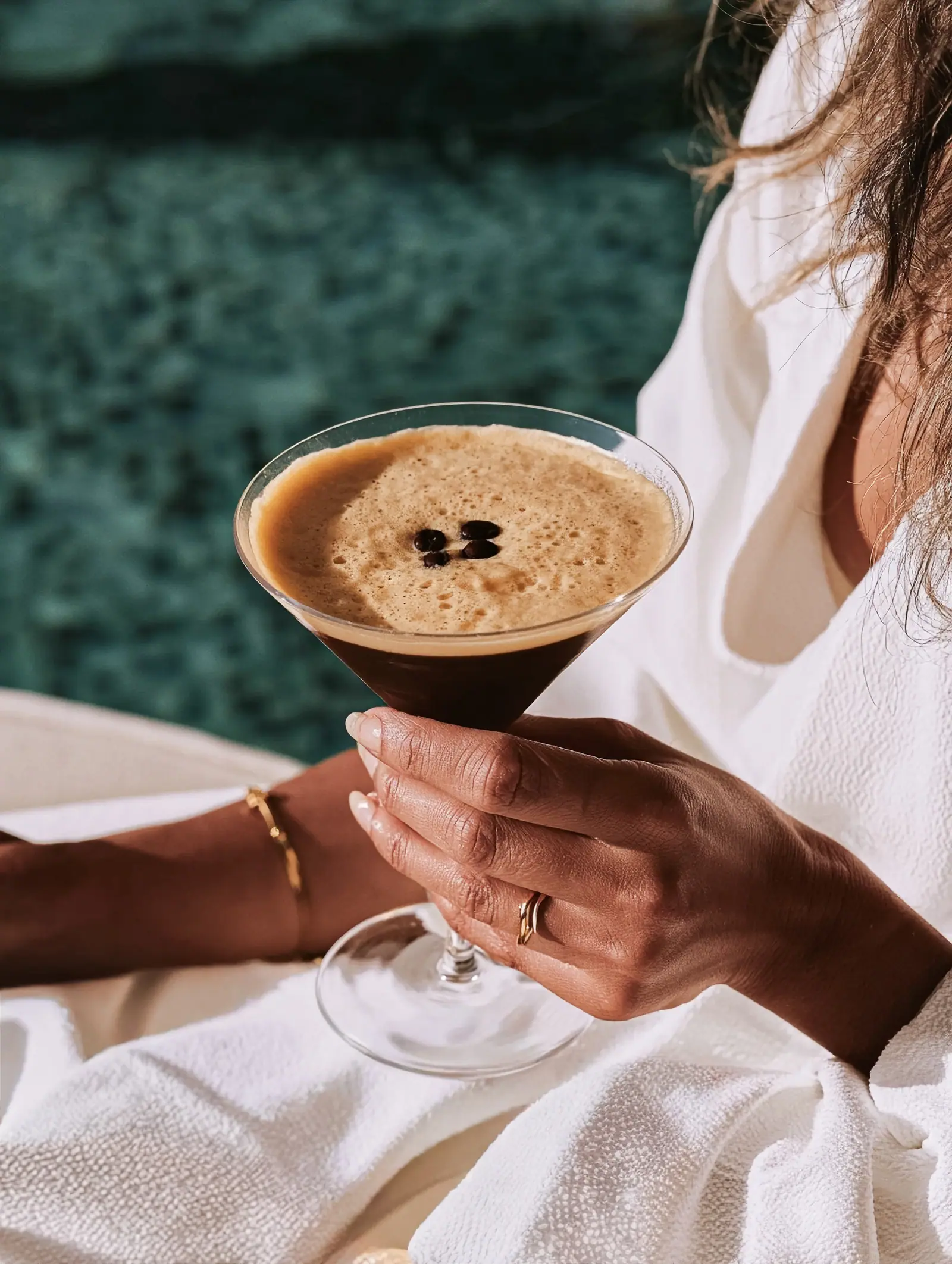 Hand holding an espresso martini beside a white robe