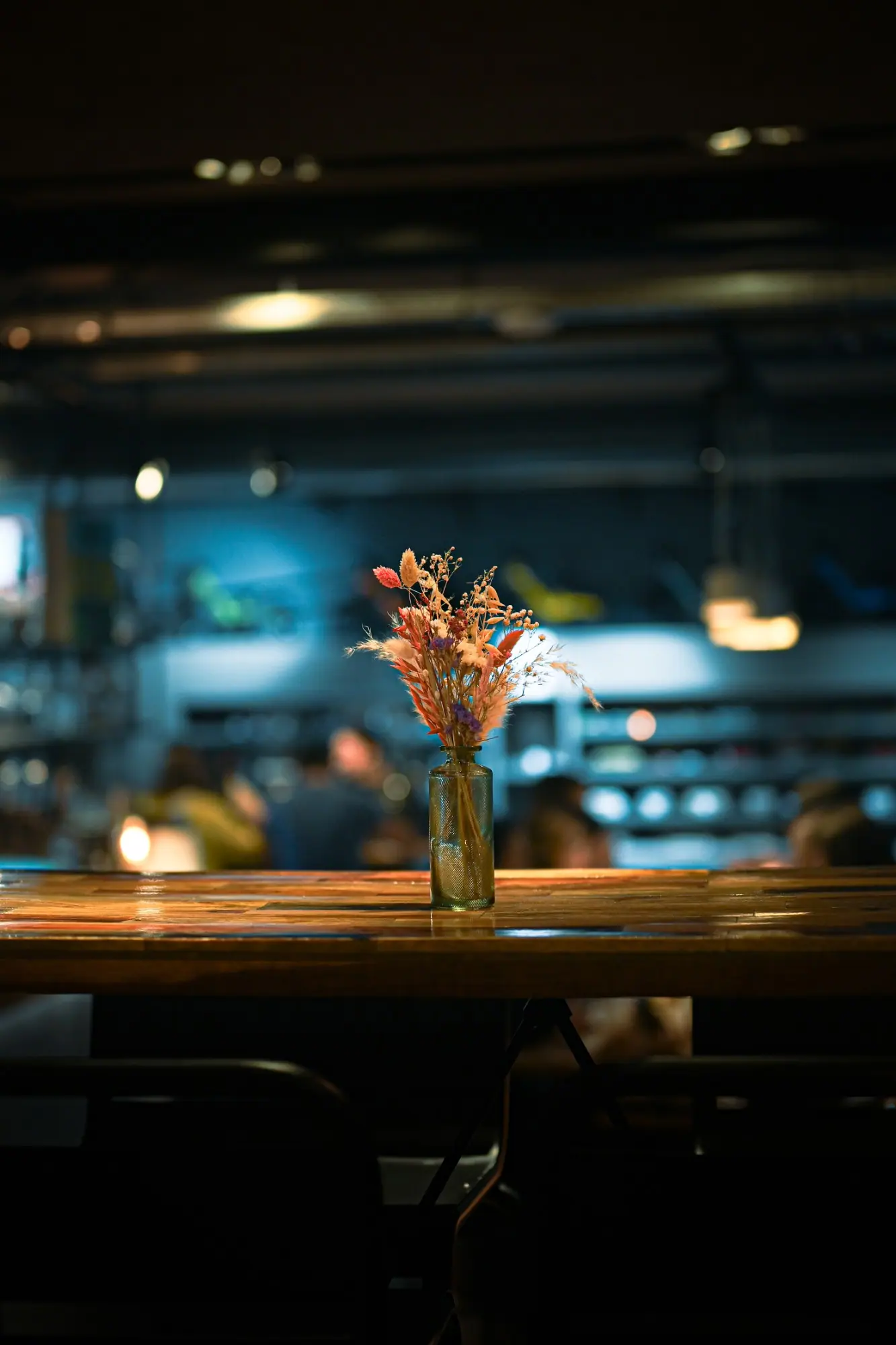 Dried flowers in a small glass bottle on a bar counter, the room out of focus behind