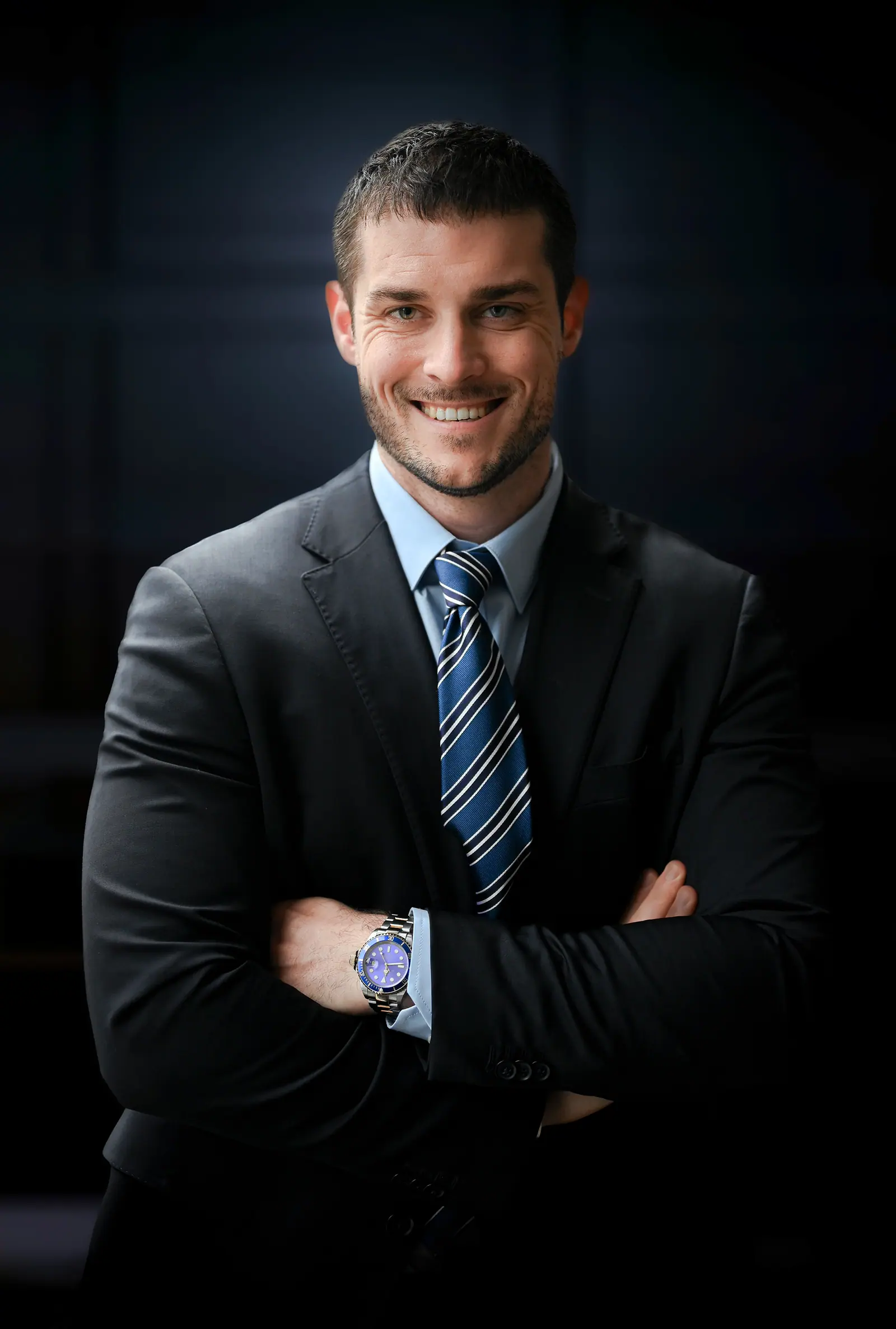 Smiling executive in a grey suit, arms crossed, against a dark backdrop