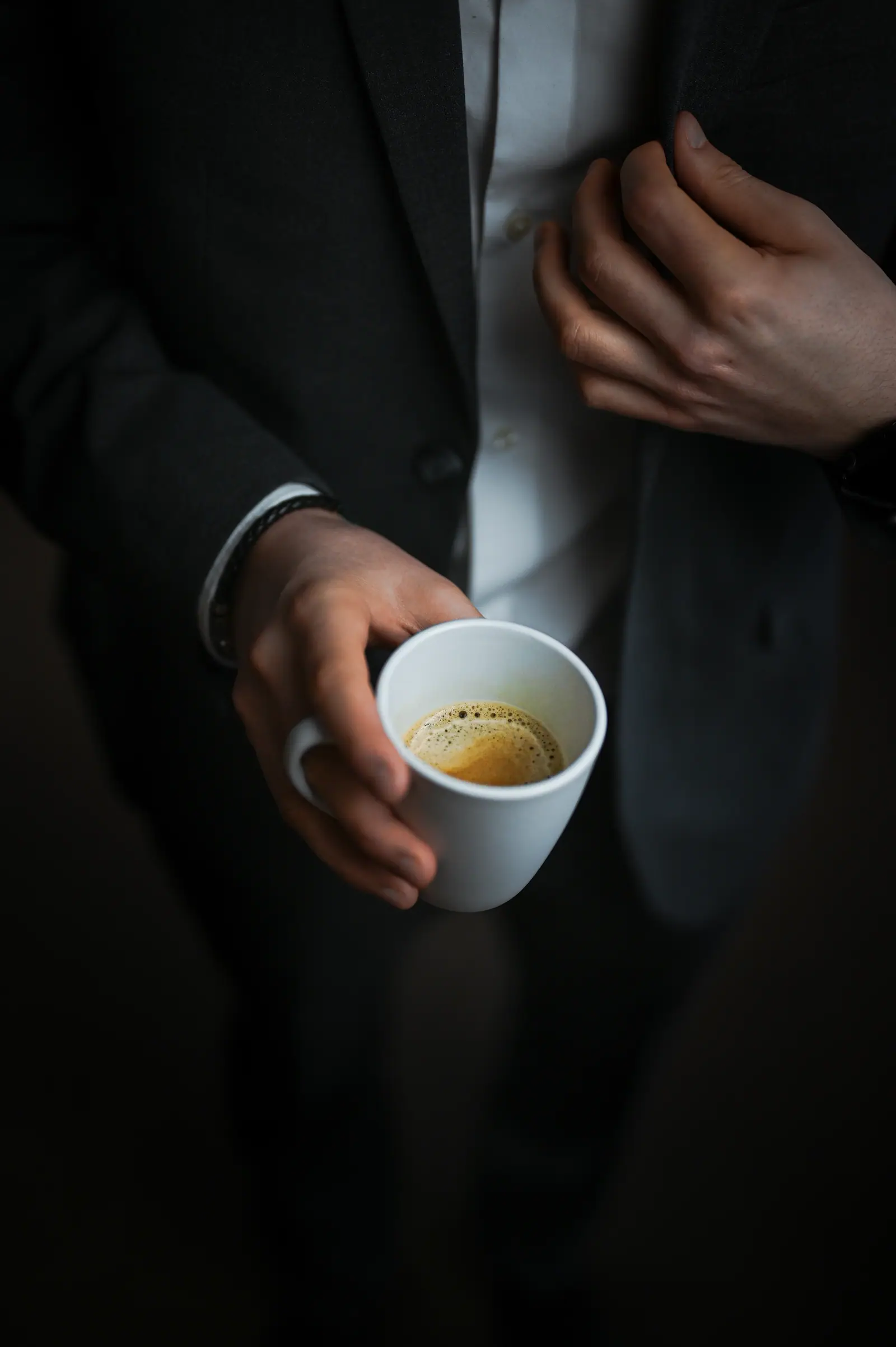 Hand holding an espresso cup against a dark suit jacket