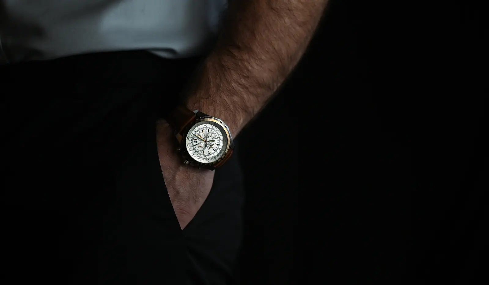 Wristwatch on a hand slipped into a trouser pocket, low light
