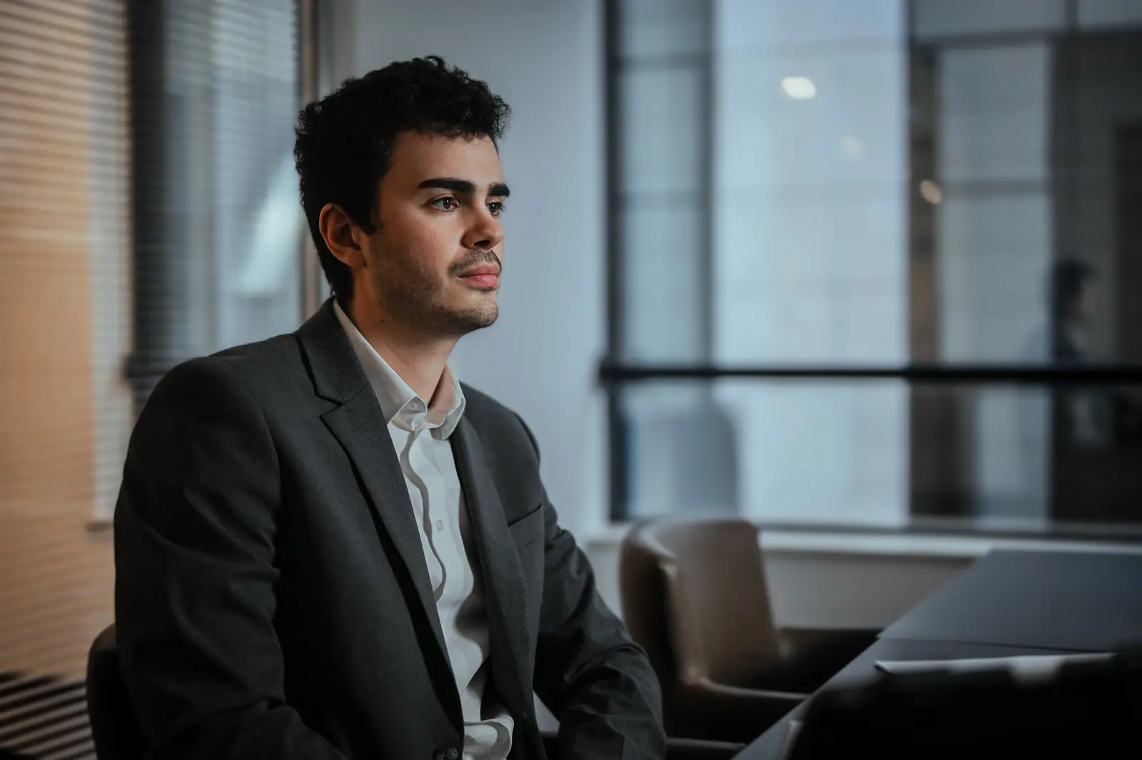 Young man in a dark suit by an office window, looking away