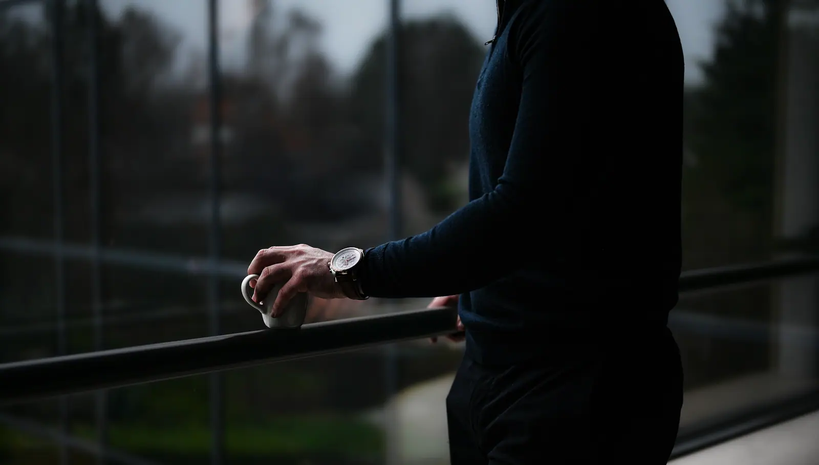 Hand with a wristwatch resting on a railing in front of a window