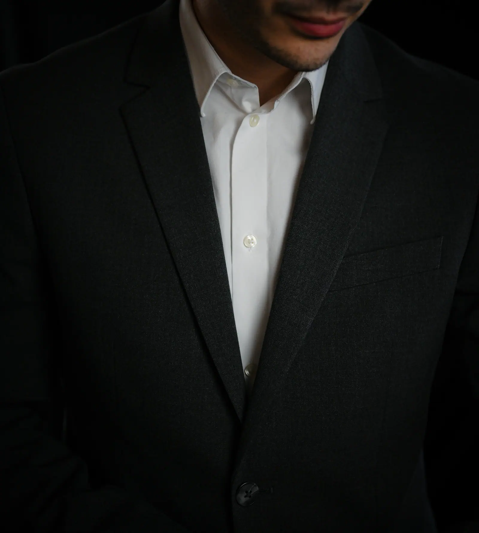 Open white collar under a dark jacket, cropped at the shoulders