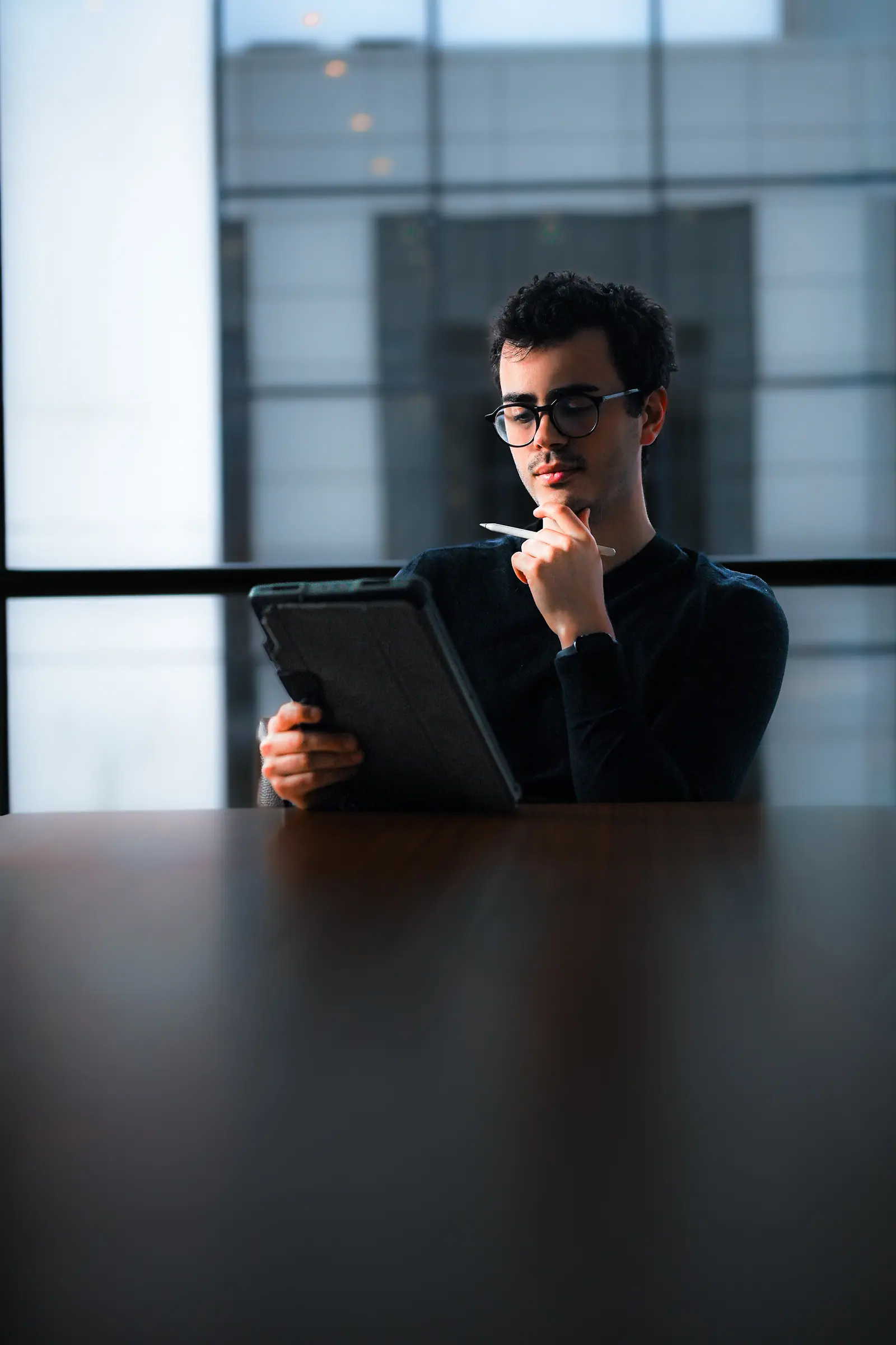 Man in glasses holding a tablet at a meeting table by the window