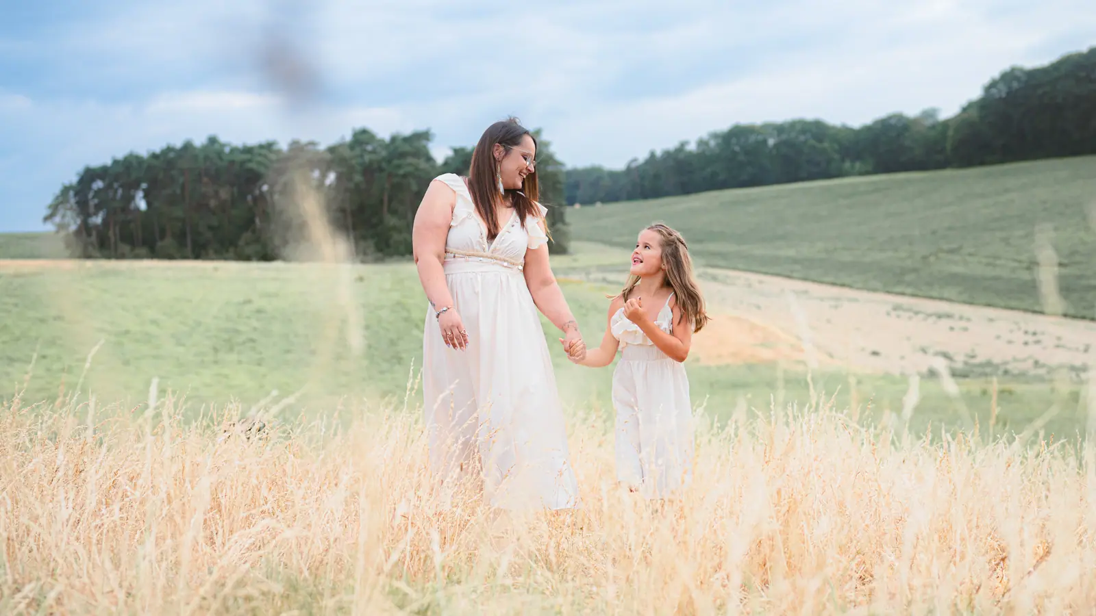 Two figures in white walking hand in hand through tall summer grass