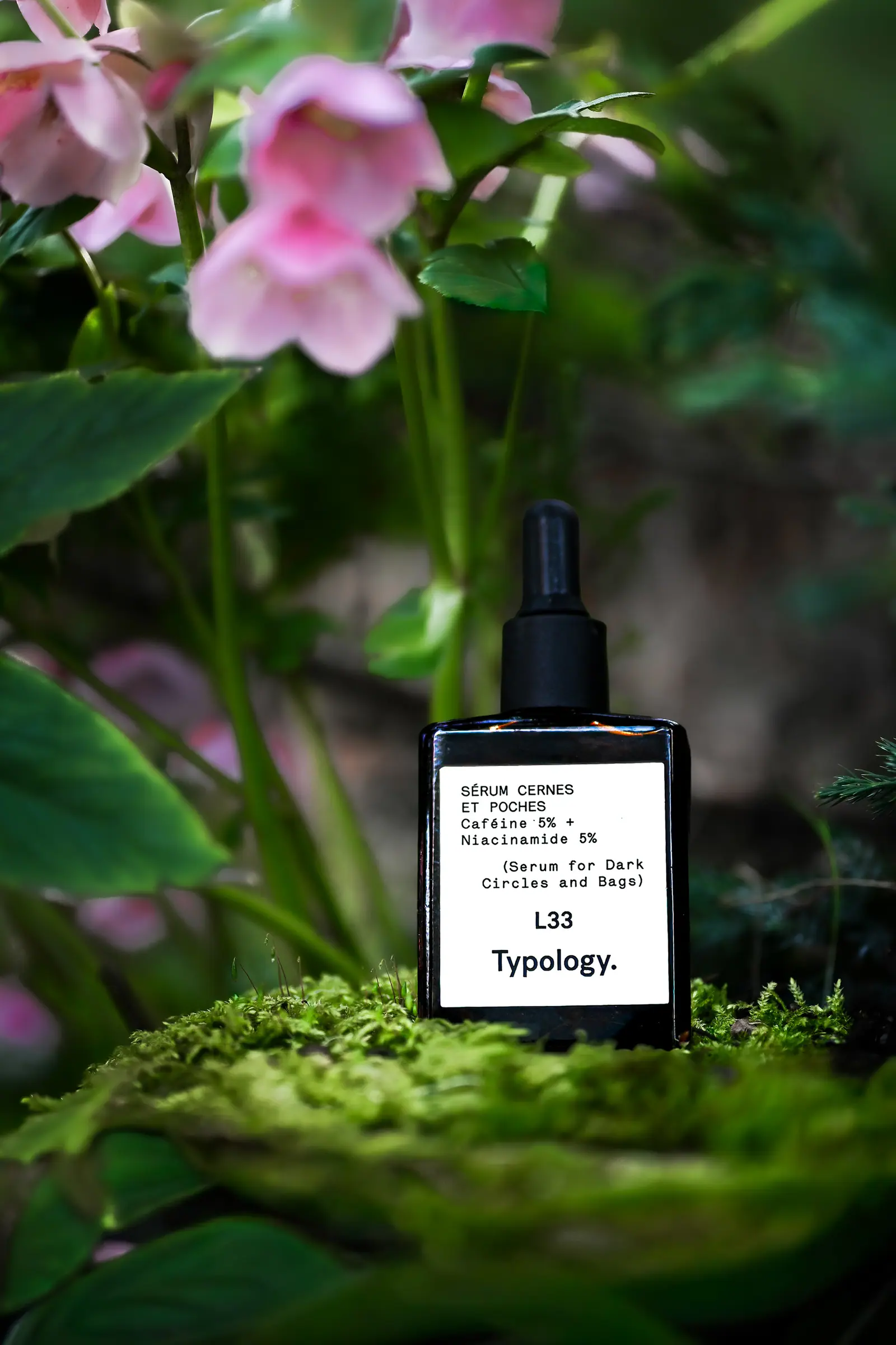 Typology serum bottle among pink flowers and moss
