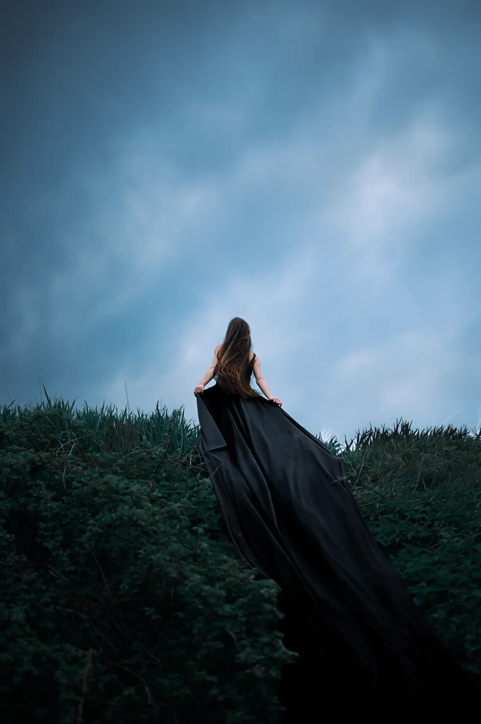 Woman in a long black gown on a hillside under a heavy sky