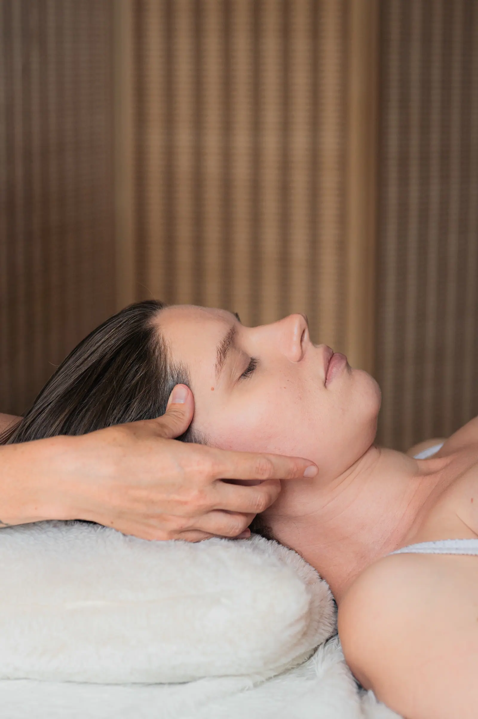 Woman lying on a massage table, eyes closed, hands at her temples